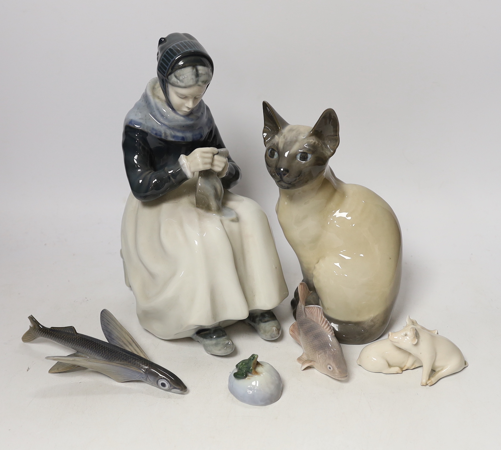 A Royal Copenhagen model of a seated lady, numbered to underside 1317, together with a further large Royal Copenhagen model of a seated Siamese cat, numbered 3281, a small group of two pigs (a.f.) numbered 1022, a seated